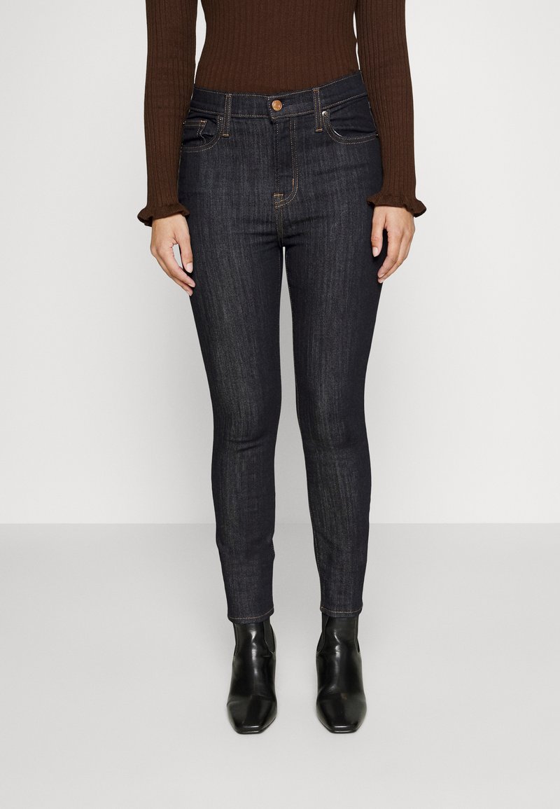 Jeans skinny de mezclilla oscura con un talle medio, que presentan cinco bolsillos, costuras a tono y se combinan con botas negras hasta el tobillo.