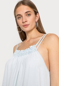 Top sem mangas azul claro com decote franzido e alças finas, apresentando um corte solto e uma textura suave. Sem padrões ou fechos visíveis.