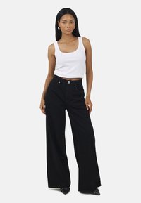 Czarne dżinsy o szerokich nogawkach i wysokim stanie, z pięcioma kieszeniami i srebrnymi akcentami, w połączeniu z dopasowanym białym topem na ramiączkach. Gładka faktura.