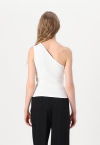 Balts, vienas pleca tops no ribotas auduma; pieguļošs stils ar elegantu dizainu. Apvienots ar augstām melnām biksēm.