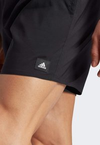 Black athletic shorts made of lightweight fabric, featuring a small Adidas logo patch and smooth texture, with a tailored fit around the thigh.