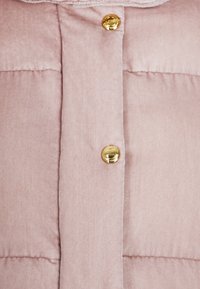Tela acolchada de un ligero color rosa con una textura suave, que presenta una fila de botones de presión dorados a lo largo de la línea central.