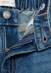 Detaljer av jeans i denim med dragkedja, blått tyg med en texturerad yta, synlig sömnad och metallknappsstängning.