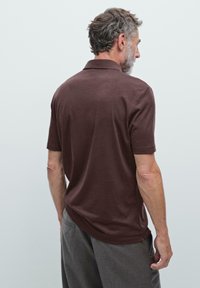 Brun polo shirt med korte ærmer, der har en klassisk krave og glat bomuldsmateriale. Set bagfra viser den en afslappet pasform og et simpelt design.