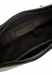Intérieur vert olive d'un sac avec une fermeture éclair noire et une doublure. Comprend une petite poche zippée et une étiquette textile rectangulaire.
