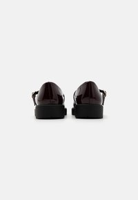 Chaussures en cuir verni bordeaux avec une semelle noire épaisse et une sangle ajustable. Texture lisse avec un design à bout rond.