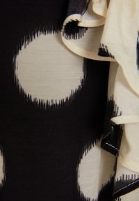 Tessuto nero e crema con grandi motivi circolari. Texture liscia con un dettaglio di volant fluttuante lungo il bordo.