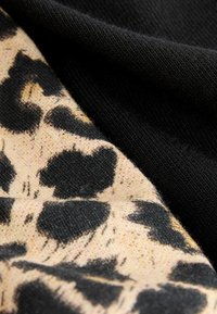 Stickad tyg med en beige bakgrund och svarta leopardfläckar, lager med enfärgad svart stickning. Slät textur med kontrasterande mönster.