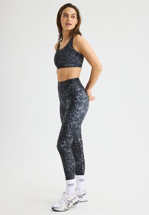 Zwart en grijs luipaardprint sportbeha en hooggerimde leggings van rekbaar materiaal. Gecombineerd met witte sokken en hardloopschoenen.