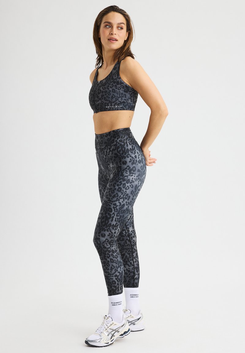 Zwart en grijs luipaardprint sportbeha en hooggerimde leggings van rekbaar materiaal. Gecombineerd met witte sokken en hardloopschoenen.