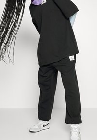 Schwarzes, übergroßes T-Shirt und Hose aus weichem Material, mit Jordan-Logos am Saum und weißen Nike-Sneakern mit grauen Akzenten.