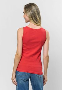 Červený žebrovaný top bez rukávů s kruhovým výstřihem a přiléhavým střihem, nošený s vysokými světle modrými džíny.