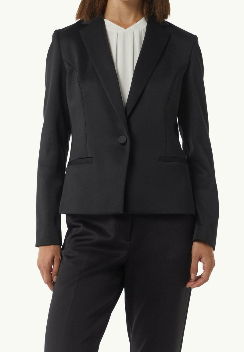 Blazer noir à coupe ajustée, avec revers encochés et fermeture à un seul bouton. Tissu lisse avec poches latérales et coutures discrètes.