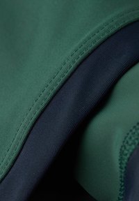 Textil in Dunkelgrün und Marineblau, mit glatten Texturen, sichtbaren Nähten und einem gefalteten Design, das die geschichteten Stoffkanten zeigt.