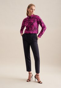 Koszula z długim rękawem w kolorze fuksji z czarnym wzorem liści; połączona z dopasowanymi ciemnymi spodniami i czarnymi sandałami na obcasie.