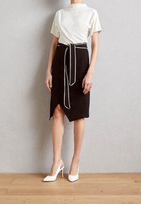 Bílý top s krátkým rukávem, spárovaný s černou sukní se zavazováním na boku a bílým lemem, doplněný bílými špičatými slingback podpatky.