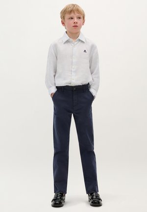 Gestreiftes weißes Hemd mit gelben Knöpfen; marineblaue Hosen; schwarze Schuhe; schlichtes Design mit Logodetails auf dem Hemd.