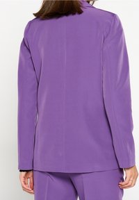 Lila kavaj med mjuk textur, enkel slits bak, långa ärmar och skräddarsydd passform, designad för en modern siluett.