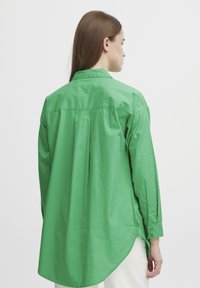 Green long-sleeve shirt made of smooth fabric, featuring a pointed collar, button cuffs, and a rounded hem with a relaxed fit.
