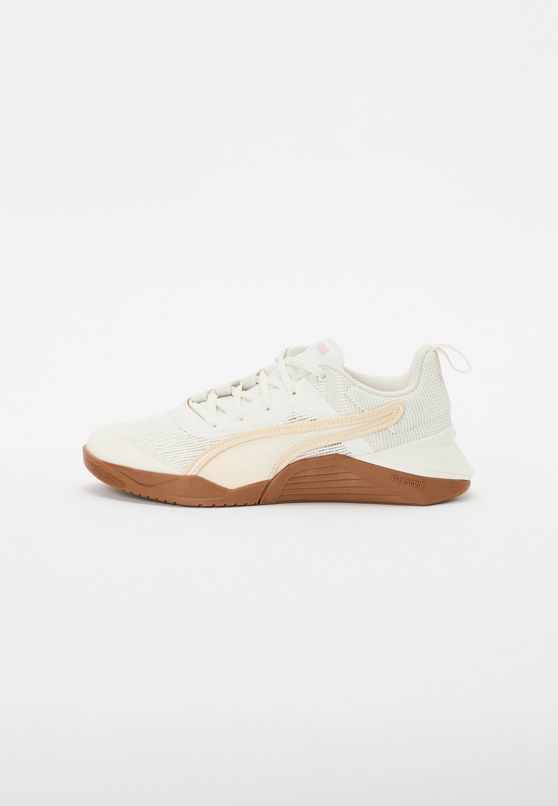 Scarpa sportiva beige chiaro con una tomaia in rete testurizzata, dettagli crema e suola in gomma naturale. Presenta lacci e un'etichetta di sollevamento sul tallone.