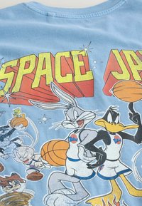 Les personnages des Looney Tunes, Bugs Bunny et Daffy Duck, en tenue de basketball, faisant tourner et tenant des ballons de basketball sous le texte en gras « SPACE JAM ».