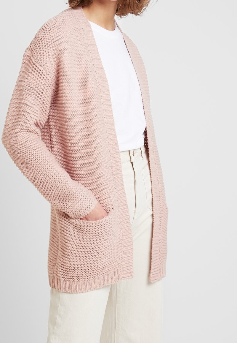Hellrosa gestrickte cardigan mit strukturiertem Muster, offener Vorderseite und zwei Seitentaschen. Lange Ärmel mit gerippten Manschetten.