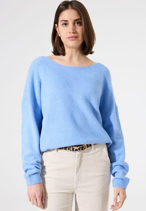 Pull de couleur bleu clair, doux, surdimensionné avec un large col et des poignets côtelés. Associé à un pantalon en velours côtelé crème et une ceinture à imprimé léopard.