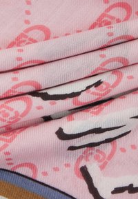 Tessuto rosa con strati piegati, caratterizzato da un motivo di cerchi rossi e linee nere. La trama appare liscia e morbida.