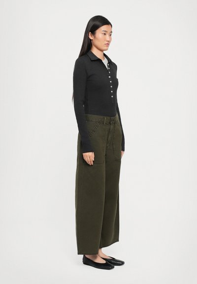 Zwarte langemouwen polo met knopen, gecombineerd met wijde olijfgroene broek en zwarte flats. De outfit heeft een relaxte pasvorm en een gestructureerde stof.