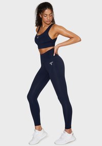 Set sportivo blu navy composto da un reggiseno sportivo aderente e leggings a vita alta, realizzati in materiale elasticizzato con una texture liscia e un dettaglio con logo.