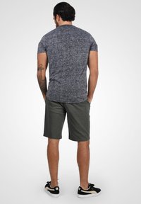 Sivi heather t-shirt s kratkim rukavima u kombinaciji s maslinastozelenim kratkim hlačama. Ima opušteni kroj i nosi se uz crne tenisice.