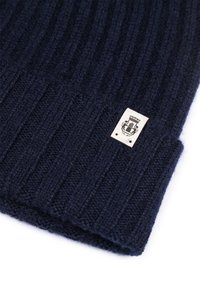 Navy blue ribbed knit fabric with a small beige rectangular label featuring a black emblem sewn onto the edge.