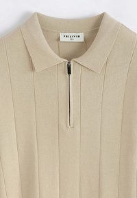 Haut polo beige côtelé avec fermeture à demi-fermeture éclair, texture douce et col à revers. L'étiquette indique "FRILIVIN", taille M.