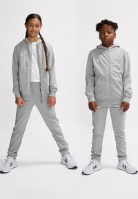 Graue Zip-Hoodies und dazu passende Jogginghosen aus weichem Stoff, ausgestattet mit Seitentaschen und weißen Akzenten. Kombiniert mit sportlichen weißen Sneakers.