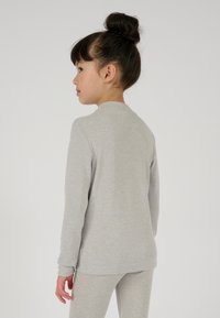 Maglietta grigia a maniche lunghe con scollatura tonda, morbido al tatto e maniche aderenti, indossata con pantaloni grigi coordinati.