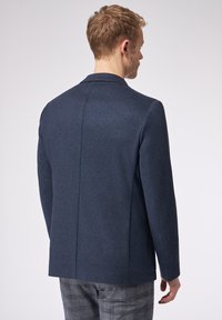 Giacca blu navy con un motivo a spina di pesce, spalle strutturate e uno spacco centrale sul retro. Vestibilità su misura, con texture del tessuto liscia.