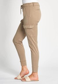 Beige Jogginghosen mit elastischem Bund, Kordelzug-Detail, Seitentaschen und gerippten Bündchen, hergestellt aus einem weichen, leichten Material.