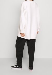 Sudadera extragrande de color blanco roto con hombros caídos, puños y dobladillo acanalados. Combinada con pantalones negros de corte cónico y zapatillas Vans negras.