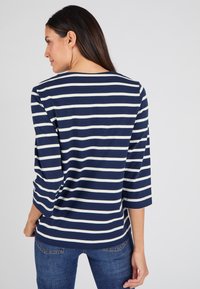 Top a righe blu navy e crema con maniche a tre quarti, scollo a giro e vestibilità comoda. Tessuto morbido e design minimalista.
