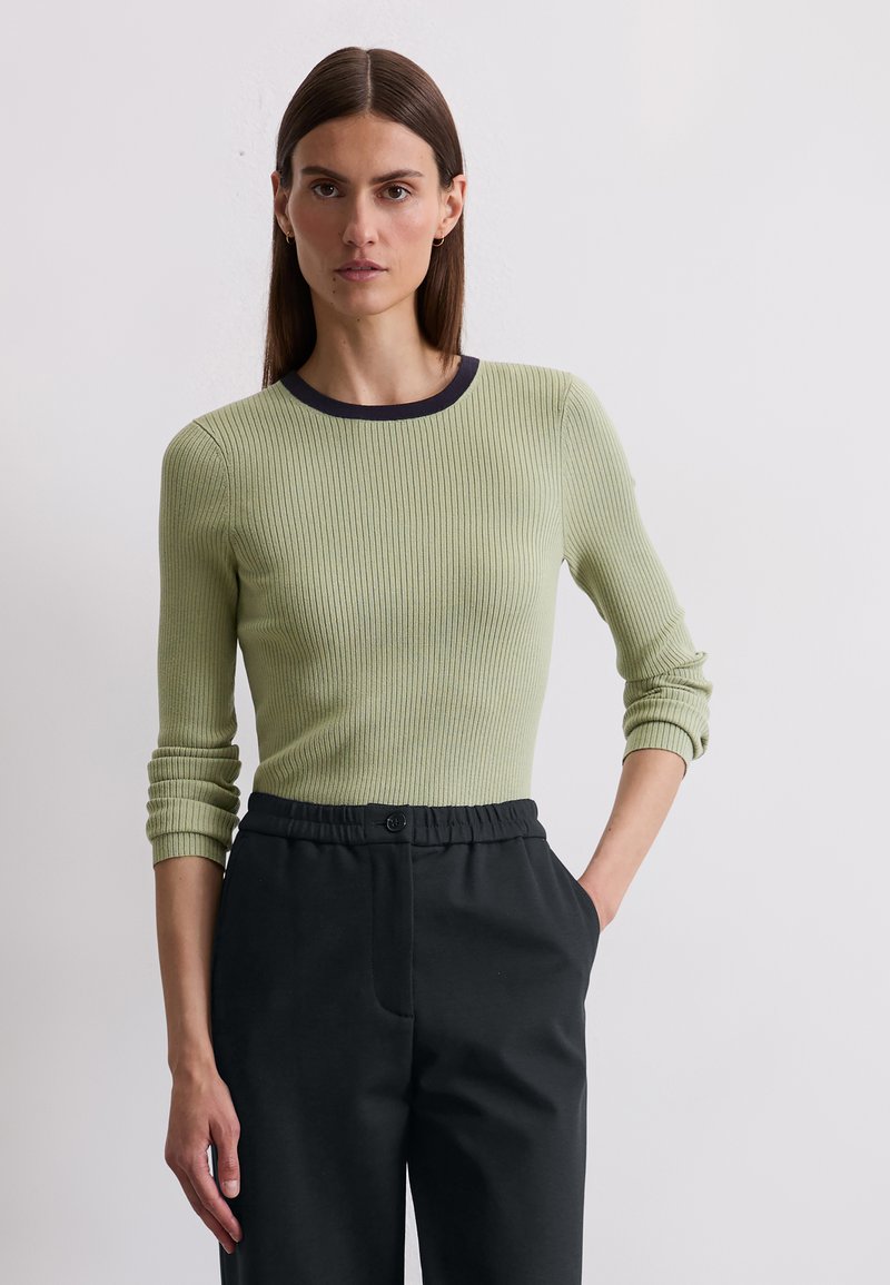 Light green ribbed long-sleeve top with a navy round neckline, paired with black trousers featuring an elastic waistband and side pockets.