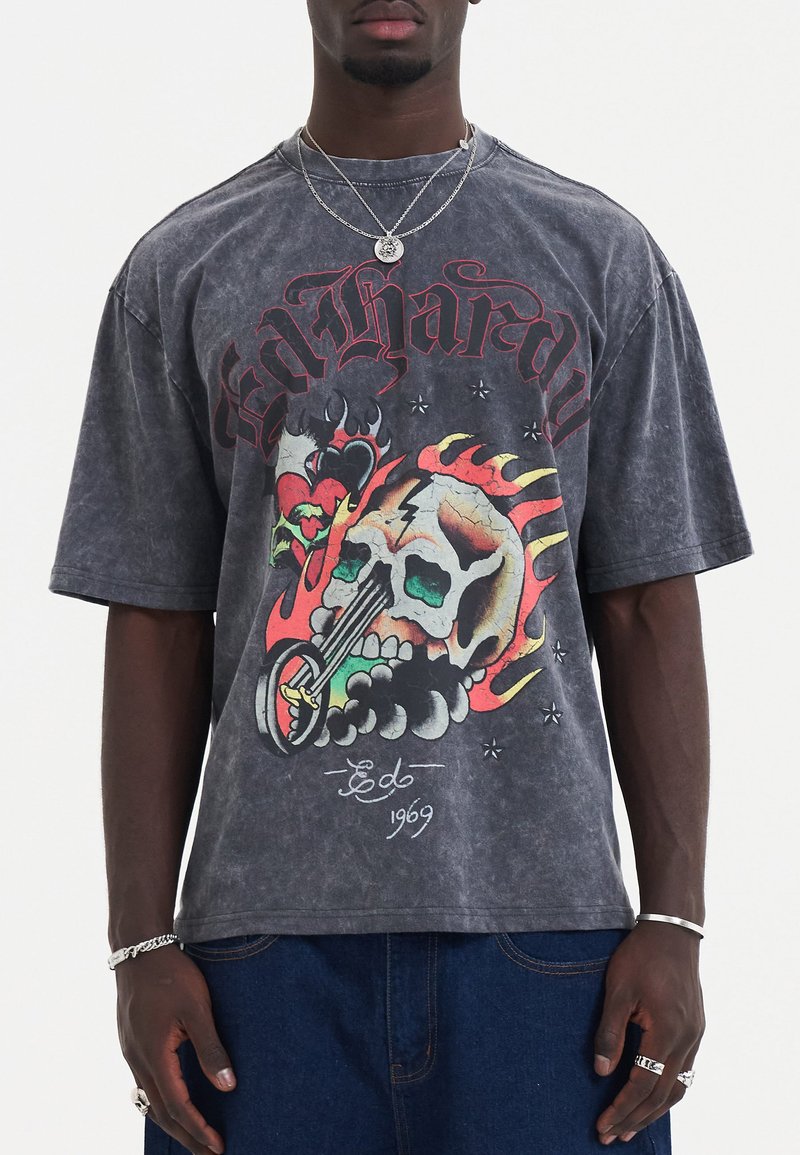 Zwarte acid-washed oversized t-shirt met een kleurrijke schedelafbeelding, vlammen, harten en tekst. Gemaakt van katoen met een zachte textuur.