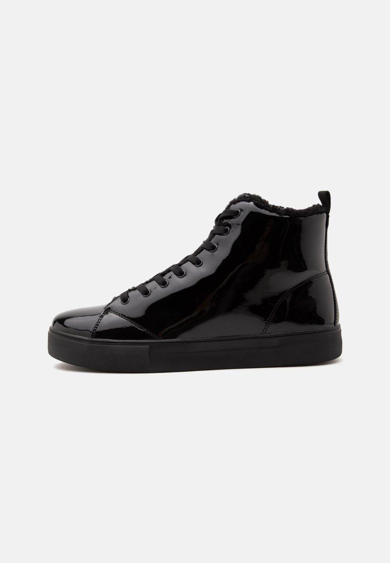 Μαύρο sneaker ψηλής πάνω με γυαλιστερό φινίρισμα, κορδόνια μπροστά, χοντρή σόλα και μαλακό επενδεδυμένο γιακά ορατό σε απλό φωτεινό φόντο.