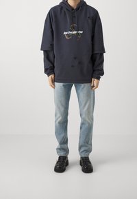 Felpa oversize blu navy con dettagli consumati e testo bianco "les benjamins", abbinata a jeans azzurri e mocassini neri chunky.
