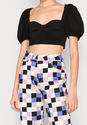 Kvinde iført en sort crop top med pufærmer kombineret med højttaljede bukser i tern i sort, hvid, lilla og lysegrøn.