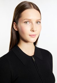 Top in maglia nera a costine con colletto e chiusura con zip davanti. La superficie liscia e il design aderente esaltano la struttura complessiva.