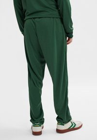 Grønne atletiske bukser lavet af glat stof, med et løst design og elastisk talje. Sammen med hvide sneakers med grønne detaljer.
