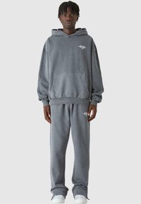 Szürke kapucnis pulóver és megfelelő sportnadrág laza szabásban, elülső zsebbel és hímzett logóval a mellrészen.