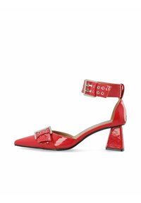 Zapato de tacón alto de charol rojo con punta afilada, tira de tobillo con detalle de hebilla plateada y tacón grueso.