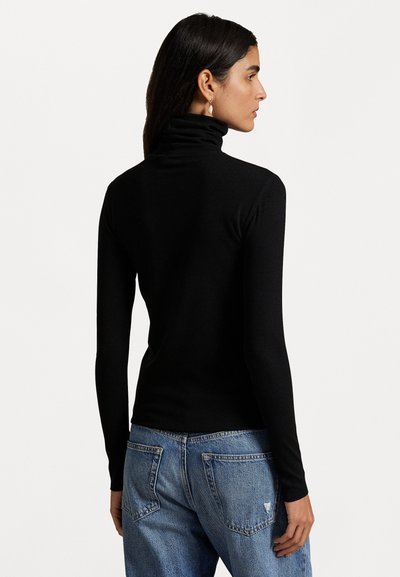 Maglione a collo alto nero a coste con maniche lunghe, design slim e colletto alto. Indossato con jeans di denim blu chiaro.