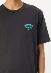 Černé bavlněné tričko s vyšitým logem "Wrangler Jeans 1947" v tyrkysové na hrudi. Krátké rukávy a kulatý výstřih.